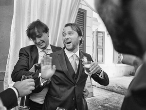 alt=The groom jokes with a friend at the wedding reception on Lake Garda